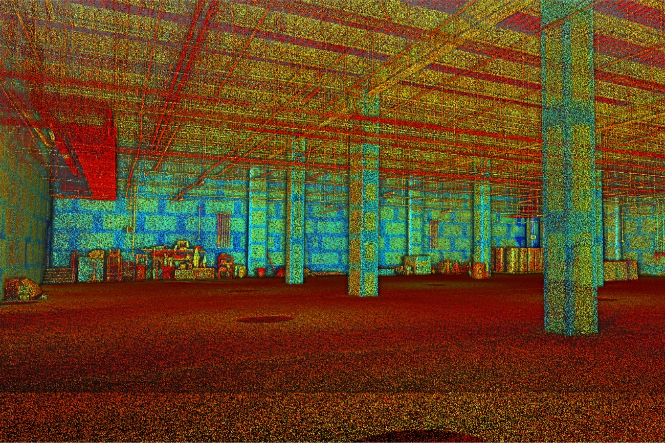 Escaneo de nube de puntos 3D colorido del interior de un almacén vacío estilo bodega, que muestra columnas, vigas y algunos objetos dispersos a lo largo de las paredes traseras y derechas, con puntos de datos rojos, azules y amarillos que delinean la estructura.