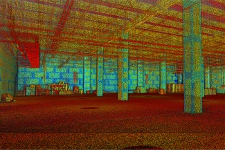 Escaneo de nube de puntos 3D colorido del interior de un almacén vacío estilo bodega, que muestra columnas, vigas y algunos objetos dispersos a lo largo de las paredes traseras y derechas, con puntos de datos rojos, azules y amarillos que delinean la estructura.