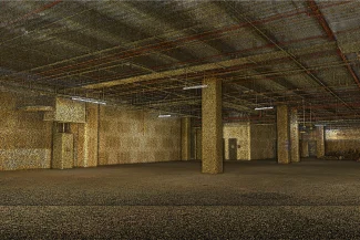 Nube de puntos de una nave industrial vacía y espaciosa, con aires de bodega, con tuberías y vigas a la vista en el techo, pilares de hormigón y una tenue iluminación fluorescente. El suelo y las paredes parecen inacabados.