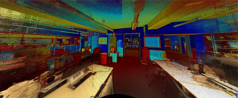 Nube de puntos de colores generada por ordenador que muestra una oficina del edificio Grimshaw con mesas, sillas, ordenadores y lámparas de techo, vista desde un extremo de la sala. Los colores van del azul y el verde al amarillo y el rojo