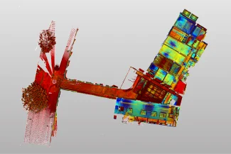 Un escaneado 3D de arriba abajo, codificado por colores, del edificio Grimshaw y la intersección de la carretera adyacente con árboles, destacando las variaciones de elevación en rojo, amarillo y azul sobre un fondo gris claro, ideal para análisis de arquitectura o construcción.