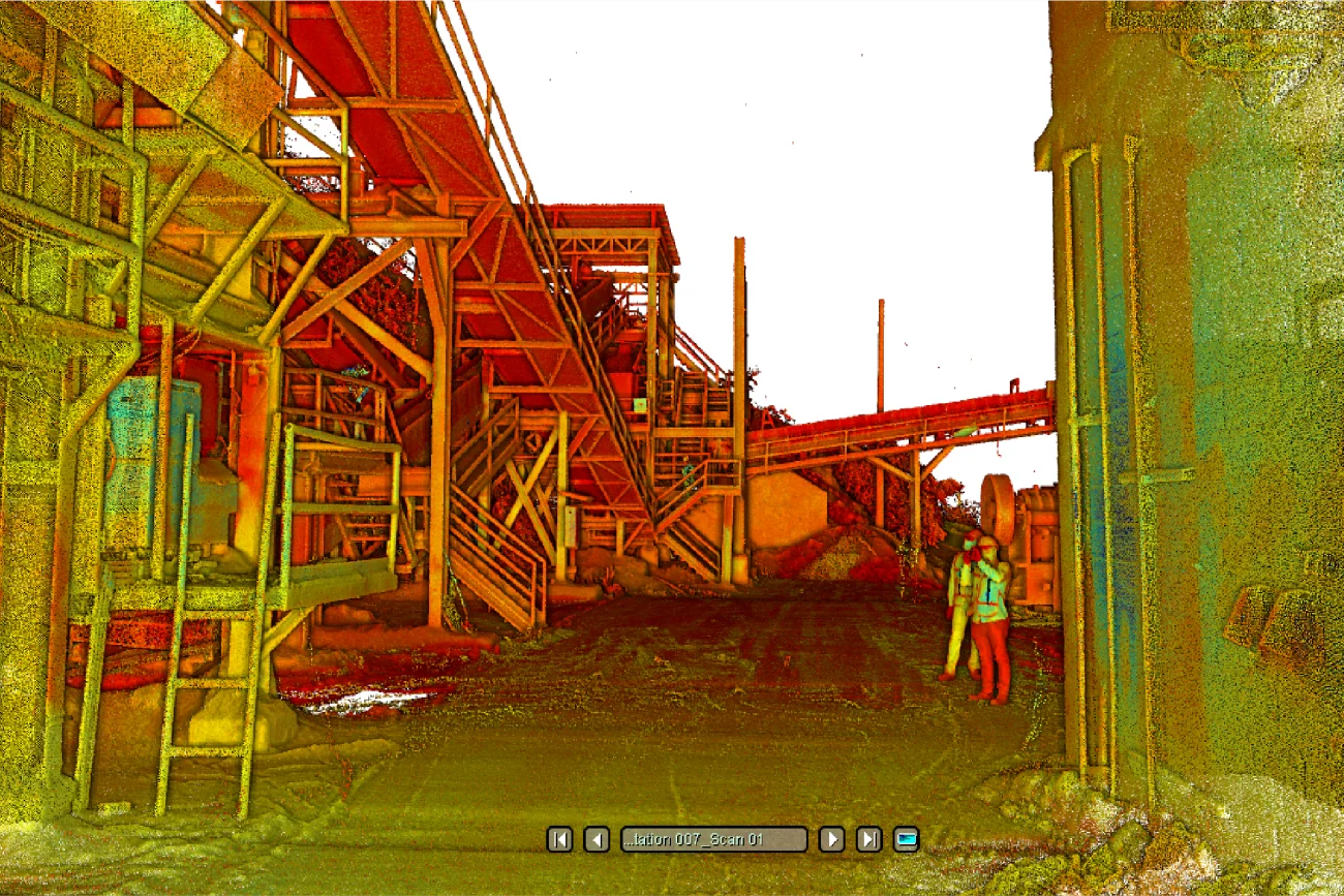 Una escena industrial distorsionada por el color en Mina DIABRAS muestra estructuras metálicas, escaleras y plataformas. Una persona con casco y chaleco de seguridad se encuentra a la derecha, cerca de un edificio. El terreno parece irregular, con escombros dispersos.