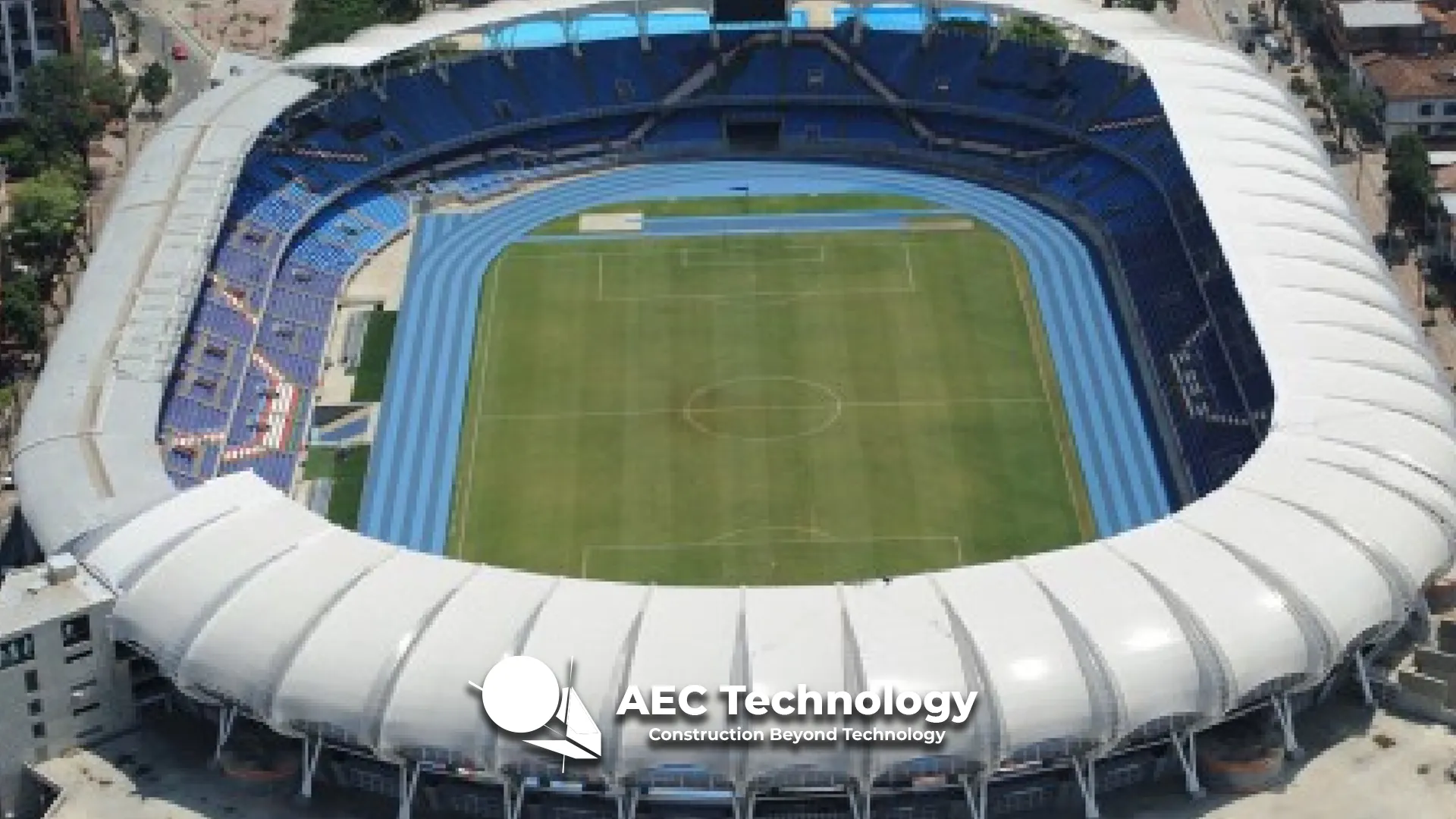 Vista aérea del Estadio Pascual Guerrero de Cali, con un campo de fútbol verde, una pista de atletismo azul y asientos azules. Destaca el techo blanco del estadio, y en la parte inferior central se ve un logotipo de AEC Technology.