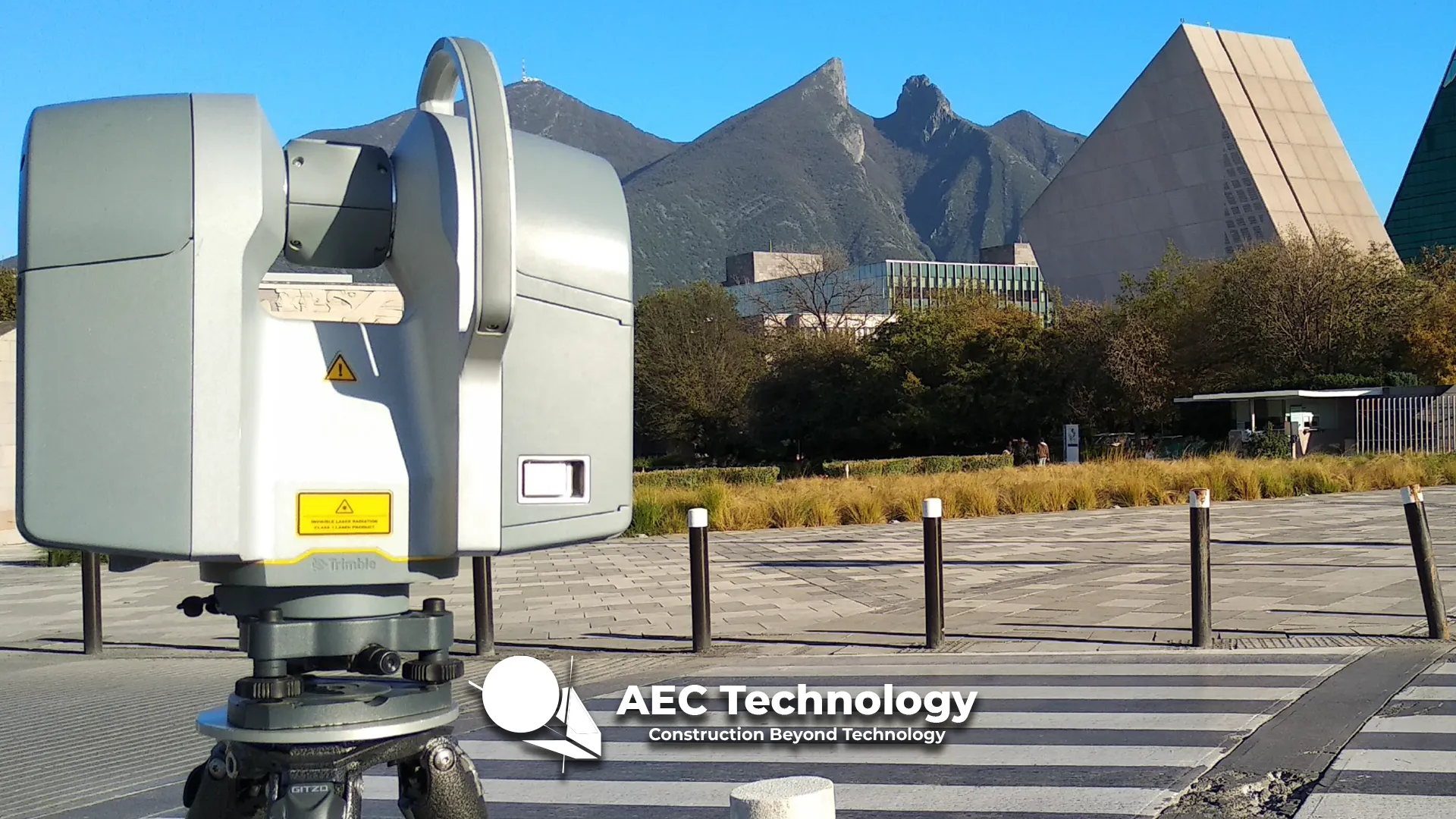 Un escáner láser 3D sobre un trípode está instalado al aire libre cerca de un moderno edificio del Tecnológico de Monterrey, con montañas al fondo. El logotipo AEC Technology Construction Beyond Technology aparece superpuesto en la parte inferior.