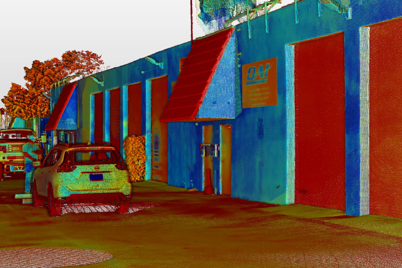 Nube de puntos coloreada muestra una calle con vehículos aparcados, un edificio industrial azul con puertas rojas y un rótulo de D&H. Bodega Overhaul, INC Los accesorios se sugieren por el entorno industrial, con árboles y vallas al fondo.