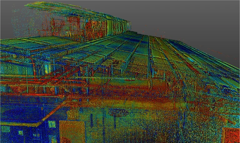 Colorida nube de puntos 3D escaneada de un gran interior de Planta Industrial, que muestra paredes, vigas y detalles del techo en tonos rojos, verdes, amarillos y azules sobre un fondo gris, capturando la vibrante estructura de las instalaciones de Mondeléz