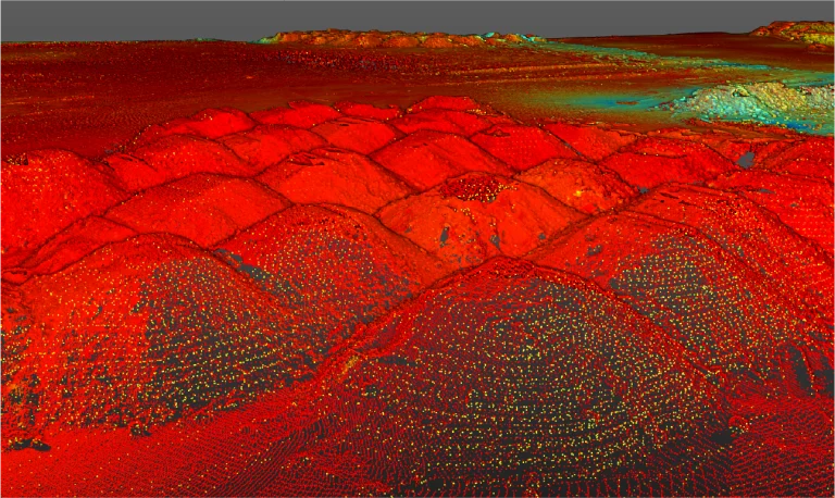 Un colorido escaneado LiDAR 3D de múltiples pilas en forma de montículo, en su mayoría de color rojo y naranja, con zonas azules y verdes al fondo, muestra detalles de elevación y superficie en un emplazamiento de Planta Industrial Nissan