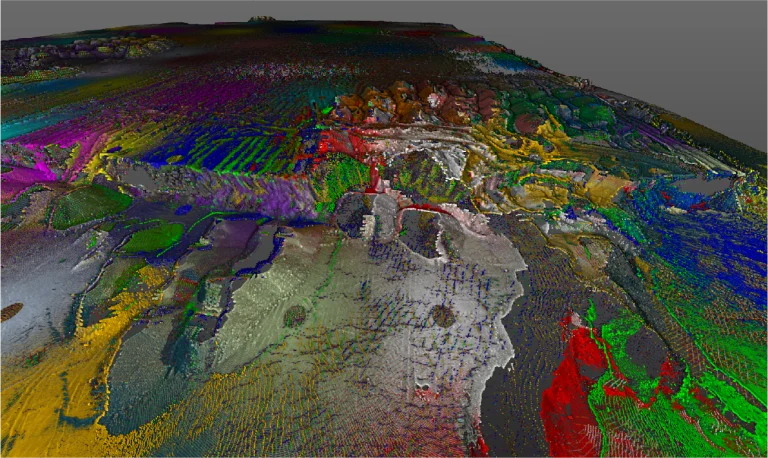 Un colorido mapa topográfico en 3D muestra diversas elevaciones y características del terreno, mostrando regiones vibrantes y texturizadas en tonos verdes, rojos, azules, morados y amarillos a través del paisaje digital de Planta Industrial Nissan