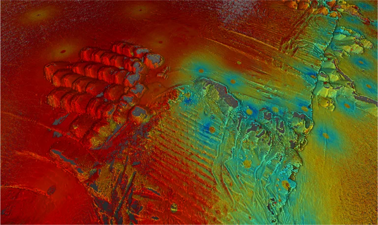 Un colorido mapa topográfico con tonos rojos, naranjas, amarillos, verdes y azules muestra los cambios de altitud alrededor de Planta Industrial Nissan. Las formas circulares y rectangulares, las líneas y las crestas destacan tanto el terreno natural como las características industriales