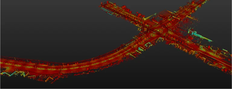 Una imagen de nube de puntos LiDAR 3D capta la Intersección Vial El Pípila, que presenta carreteras curvas e intersectadas bordeadas de edificios y árboles. Los vibrantes puntos rojos, verdes y azules destacan sobre un fondo oscuro