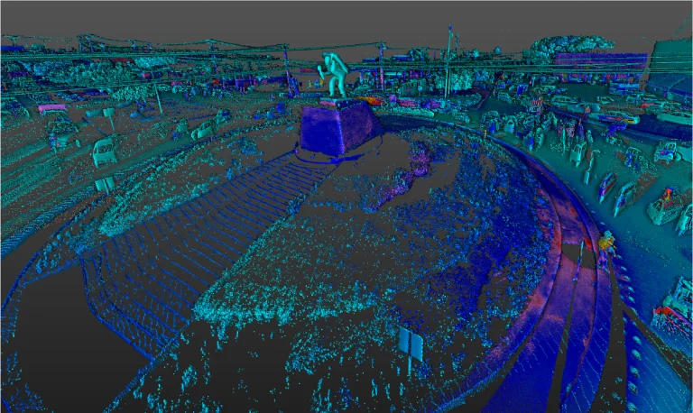 Nube de puntos Vista aérea de la Intersección Vial El Pípila, con una gran estatua sobre un pedestal en su centro, rodeada de carreteras con coches y vegetación. La escena parece tomada en una zona urbana con varios edificios cercanos
