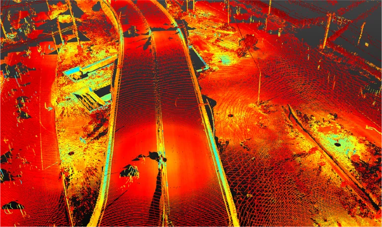 Una imagen de nube de puntos de arriba abajo generada por LiDAR muestra la Intersección Vial de las calles Kennedy y Lincoln, con colores rojo, naranja y amarillo que representan la elevación. Los elementos de la carretera, los vehículos, las infraestructuras y el paisaje circundante aparecen superpuestos en forma de malla