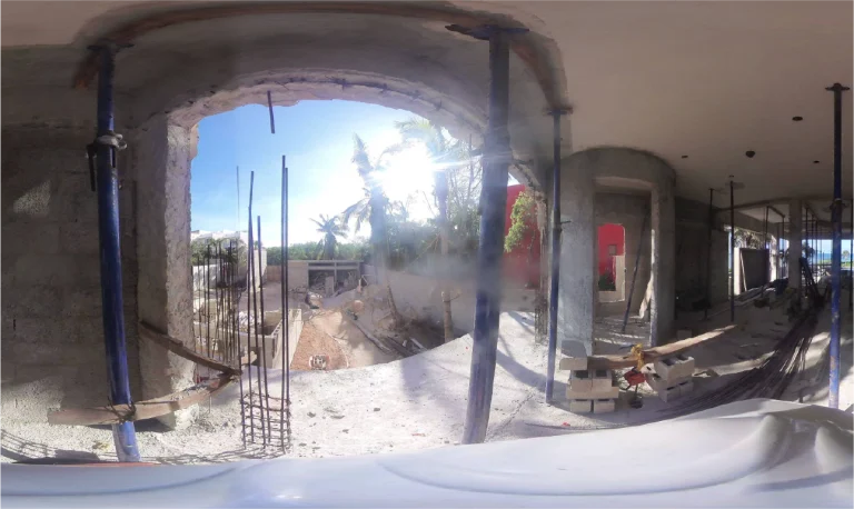 Una vista de 360 grados de un edificio en construcción, muestra muros de hormigón visto, andamios metálicos, huecos de ventanas por los que entra la luz del sol y palmeras en el exterior. En el interior hay materiales de construcción y escombros esparcidos