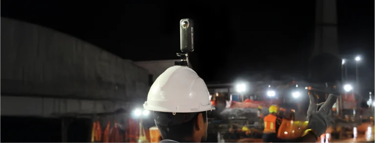Una persona que lleva un casco blanco con una cámara montada en la parte superior se encuentra en una obra de construcción por la noche