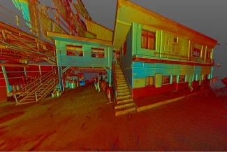 A colorful 3D point cloud scan of the Tamazula Sugar Mill in Jalisco, showing the exterior of a two-story industrial building with stairs, metal pipes, and several people standing on a textured floor, capturing the essence of sugar production.