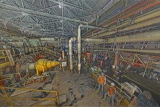 Inside the Tamazula Sugar Mill in Jalisco, an industrial facility bustles with workers in safety gear tending to large pipes and machinery, all dedicated to producing sugar under a high, open roof.