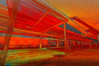 Nube de puntos de una estación de autobuses o trenes moderna y vacía del Aeropuerto Internacional de Guadalajara, con vigas metálicas y un tejado parcialmente cubierto, bañada en intensos tonos rojos, naranjas y amarillos.