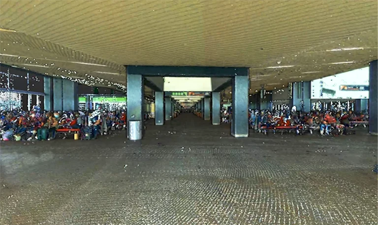 Nube de puntos de gran sala de espera cubierta en el Aeropuerto Internacional de Tijuana, con hileras de bancos y mucha gente sentada bajo el alto techo acanalado, mientras los pasillos abiertos se extienden en la distancia