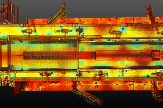 Una vista desde arriba de una imagen de escaneado láser en 3D del Aeropuerto Internacional de Tijuana muestra una estructura industrial rectangular en colores infrarrojos, que pasan del rojo y el amarillo al azul, resaltando las variaciones de temperatura o elevación.