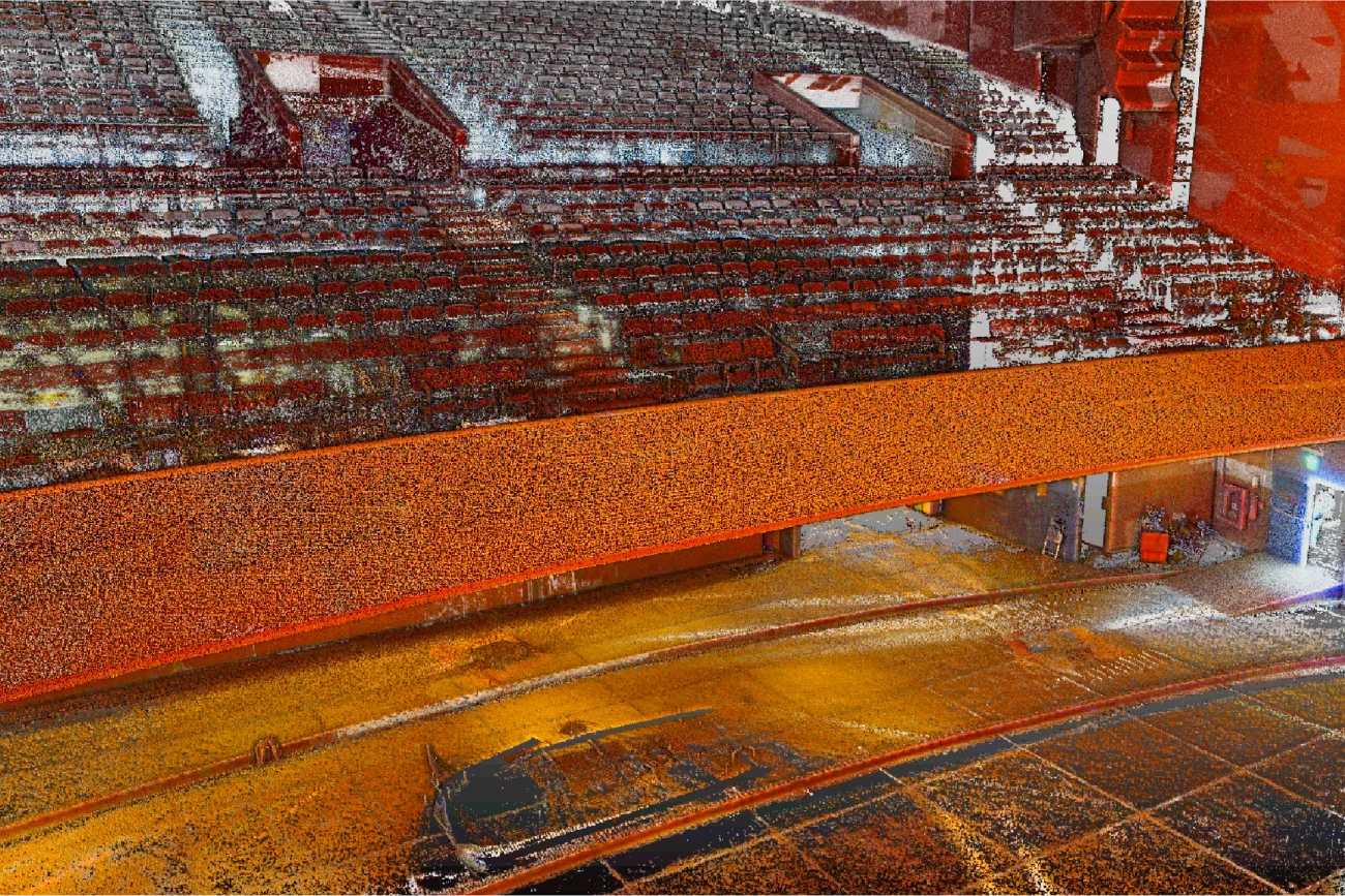 Nube de puntos del Auditorio Blackberry, presenta gradas vacías, un amplio escenario y un balcón naranja. La imagen aparece granulada y pixelada, con una luz brillante que brilla desde una puerta a la derecha para crear un efecto abstracto.