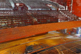 Nube de puntos del Auditorio Blackberry, presenta gradas vacías, un amplio escenario y un balcón naranja. La imagen aparece granulada y pixelada, con una luz brillante que brilla desde una puerta a la derecha para crear un efecto abstracto.