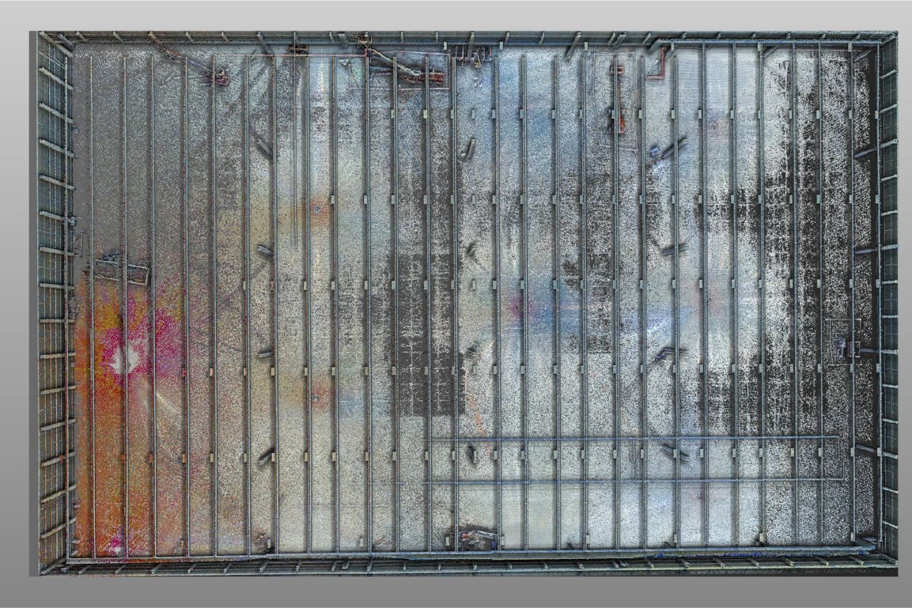 An aerial view of a rectangular enclosed area at the BMW Industrial Plant, with people walking across a floor covered in colorful dust and patches of black, orange, and white, creating a vivid, abstract pattern.