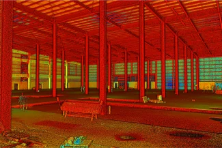 Imagen en color de un gran almacén vacío en Mitikah, con columnas, vigas y soportes de techo rojos. Hay materiales de construcción y escombros esparcidos por el suelo de hormigón, lo que apunta a su futura transformación en una sala de cine Cinépolis.