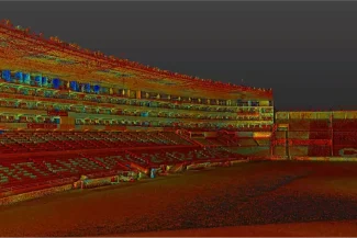 A large, empty football stadium with several tiers of red seats and bright lights illuminating the stands at night. The pitch is dark, and the scoreboard glows in the background at the Nou Camp Stadium.