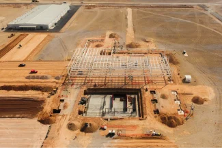 An aerial view of the BMW Industrial Plant construction site, featuring the steel structure of a building under construction, surrounded by dirt, construction vehicles, and nearby completed buildings.