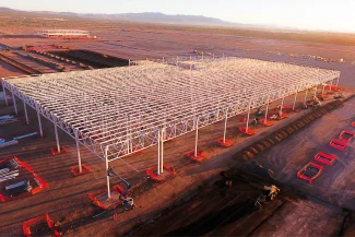 An aerial view of the BMW Industrial Plant construction site, featuring a steel structure under construction, surrounded by construction materials, machinery, and soil in an open landscape.