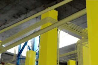 A view of several yellow structural columns and white pipes inside the Sentura Tlalnepantla Shopping Center, showing an industrial setting with a concrete ceiling and exposed structure.