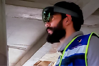 A bearded man wearing a smart headset and a reflective safety vest stands inside the Sentura Tlalnepantla Shopping Center, possibly at a construction site, looking ahead.