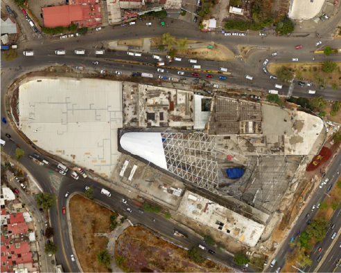 Aerial view of the large, partially constructed Sentura Shopping Center with a geometric roof, surrounded by busy roads and some vegetation in Tlalnepantlas urban landscape