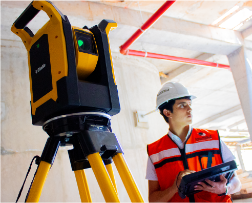 Un trabajador de la construcción con casco y chaleco de seguridad usa una tableta junto a un dispositivo de escaneo láser montado en un trípode amarillo dentro del inacabado Centro Comercial Sentura en Tlalnepantla