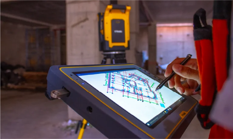 Una persona utiliza un lápiz en una tableta digital que muestra un plano del edificio en el sitio de construcción del Centro Comercial Sentura en Tlalnepantla, con equipo de topografía instalado en el fondo