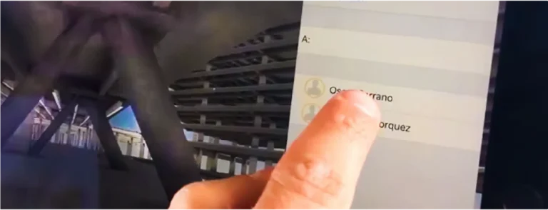 Un primer plano de un dedo que señala el nombre de Oscar Serrano en un dispositivo de pantalla táctil, con una estructura arquitectónica