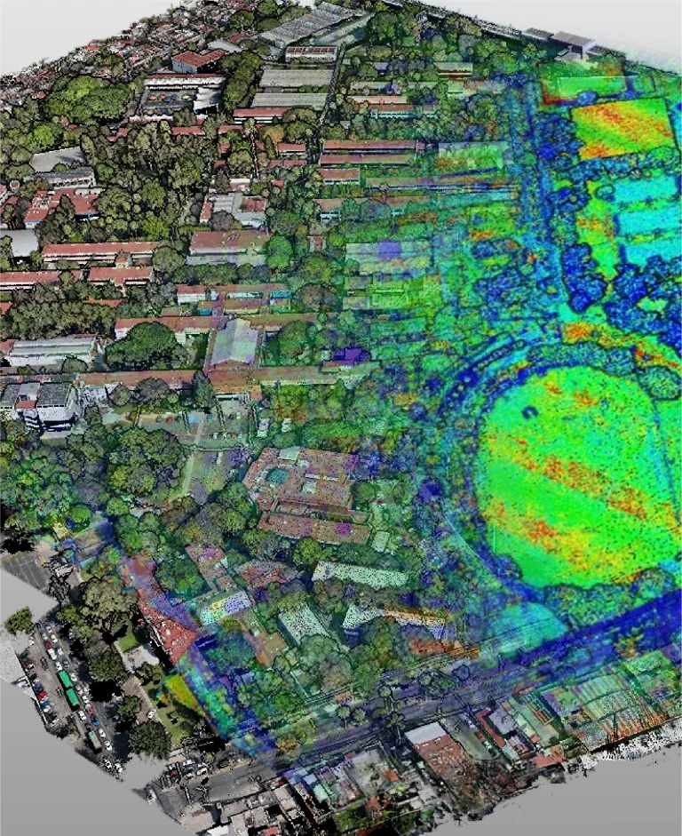 Vista aérea de una zona urbana con edificios y árboles, parcialmente superpuesta por una nube de puntos en color mejorado con LiDAR, que indica niveles variables en todo el paisaje.