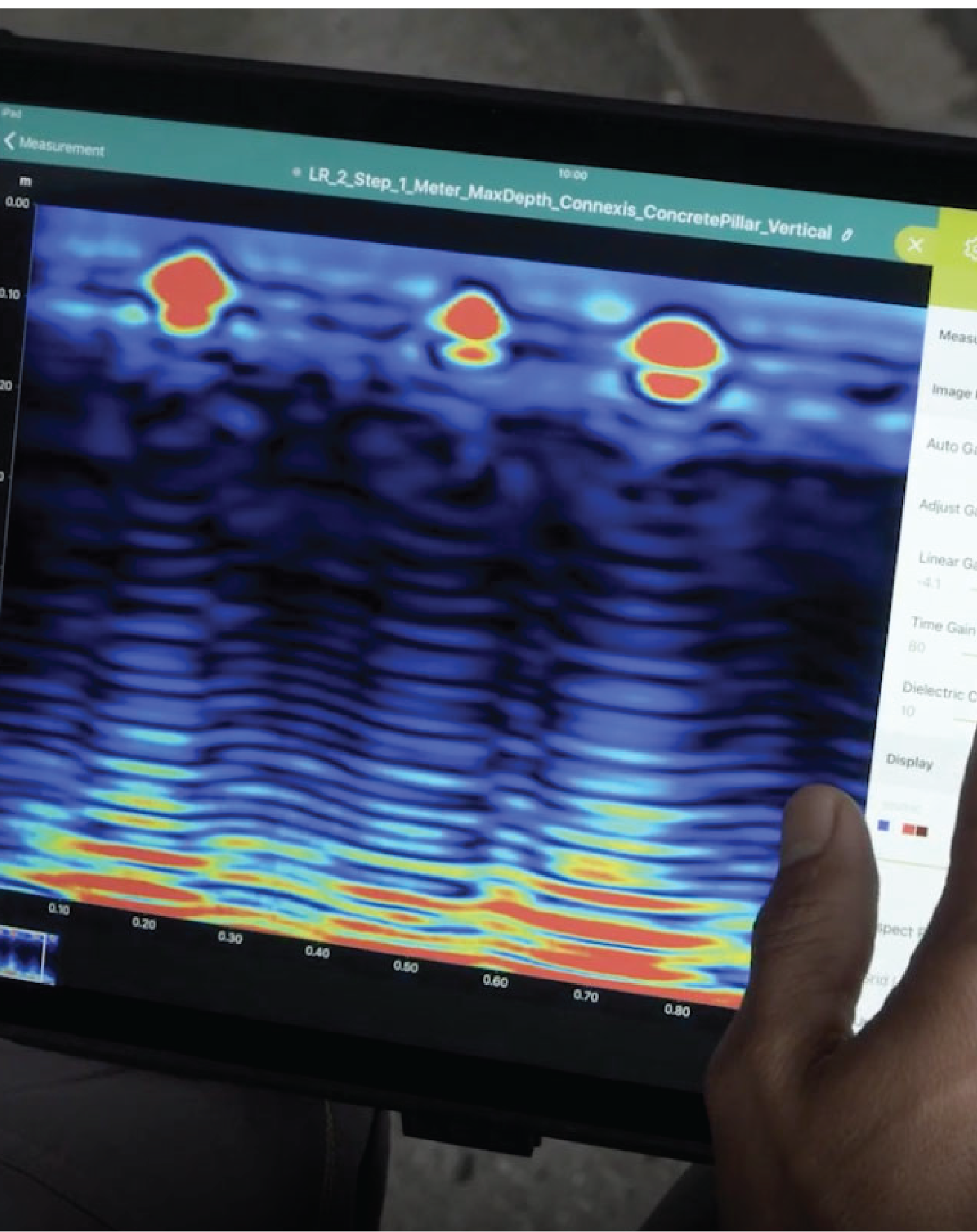 Una persona sostiene una tableta en la que se muestra un escáner de radar en color con puntos calientes rojos y amarillos sobre un fondo azul y negro, utilizando tecnologías avanzadas para documentar el entorno físico para una inspección estructural detallada.