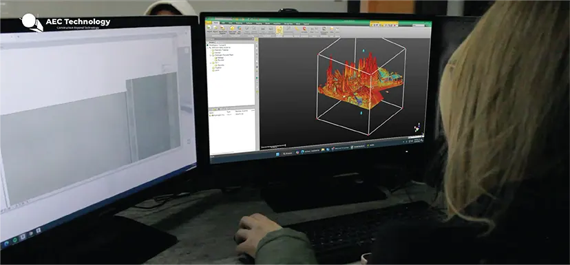 Una persona utiliza dos monitores; el izquierdo muestra software arquitectónico basado en tecnologías avanzadas, mientras que el derecho exhibe una visualización 3D de datos con coloridos picos rojos para documentar el entorno físico.