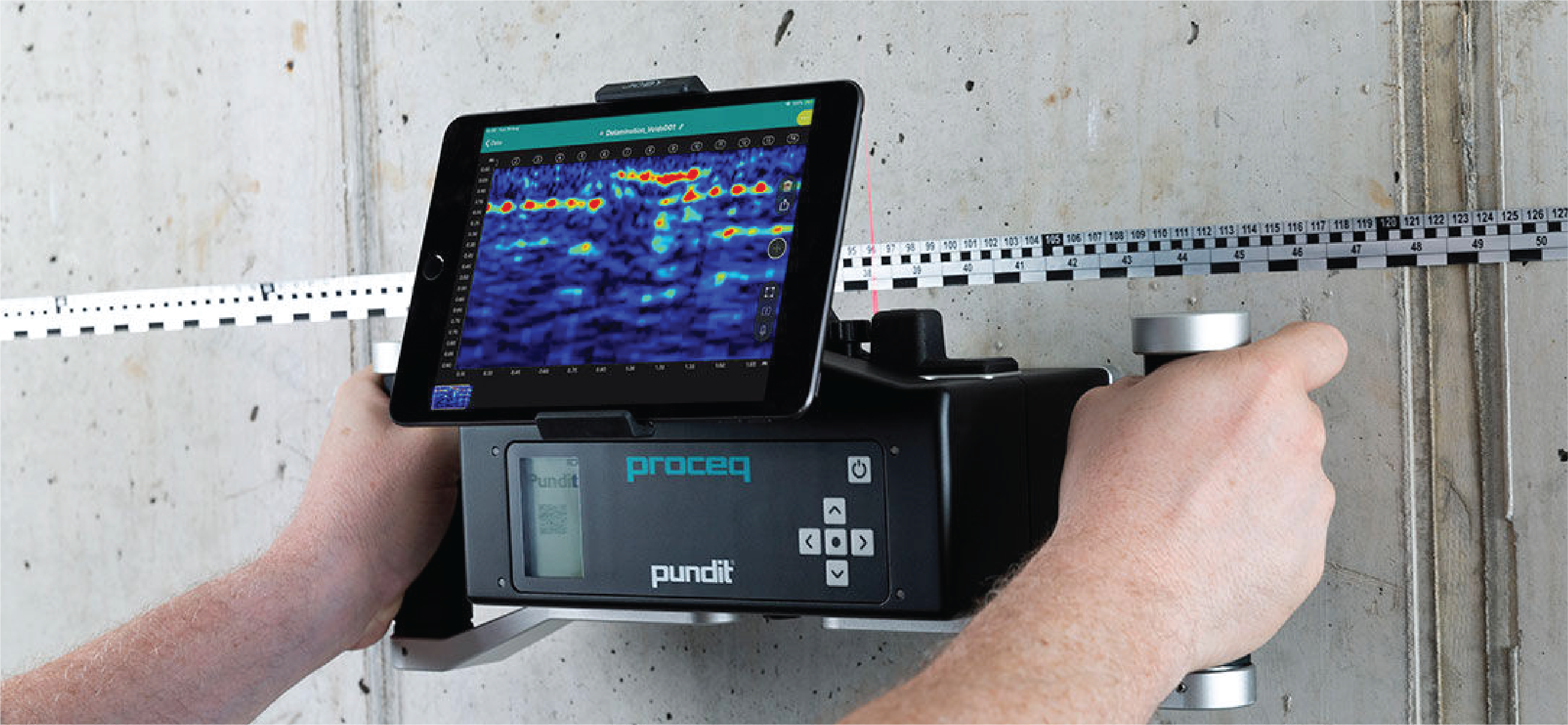 Una persona utiliza un dispositivo Proceq Pundit con una tableta conectada para escanear y analizar el interior de un muro de hormigón, empleando tecnologías avanzadas para la captura de la realidad y la visualización de datos digitales en la pantalla de la tableta.