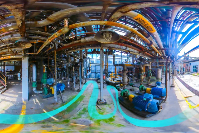 Una Fotografía Digital Técnica capta una vista de 360 grados de una instalación industrial con numerosas tuberías, válvulas, maquinaria y grandes motores azules. La zona aparece erosionada por el óxido cuando la luz del sol se filtra a través de la estructura metálica superior.