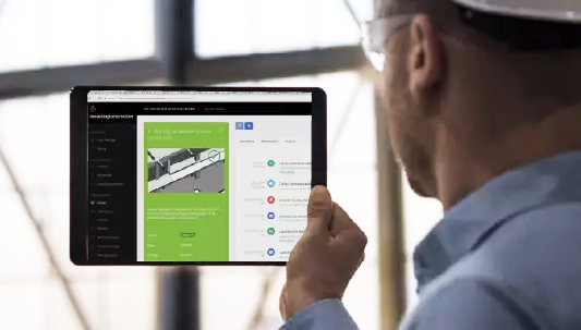A person wearing a hard hat and safety glasses holds a tablet displaying a construction project management interface with data science-driven diagrams and checklists.