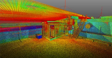 Una colorida nube de puntos LiDAR 3D escaneada de una zona industrial interior, que muestra una escalera, barandillas, maquinaria y diversas superficies en vibrantes tonos rojos, amarillos, verdes y azules.