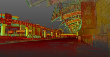 Una pasarela cubierta con una estructura geométrica de techo metálico se extiende a lo largo de un edificio moderno por la noche, iluminada por luces y mostrada a través de Escaneo LiDAR CDMX, con una zona pavimentada vacía en primer plano.